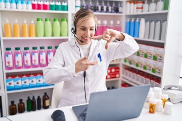 Young caucasian woman working at pharmacy drugstore using laptop smiling making frame with hands and fingers with happy face. creativity and photography concept.