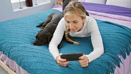 A young caucasian woman enjoys leisure time with her labrador dog in a cozy bedroom using a...