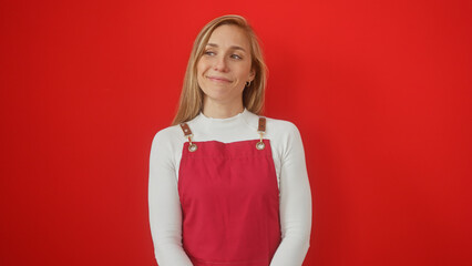 Smiling blonde woman in white top and red overalls against a solid red background