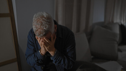 Obraz premium Despondent handcuffed senior man contemplates legal documents in a dimly lit room, portraying distress and legal trouble.
