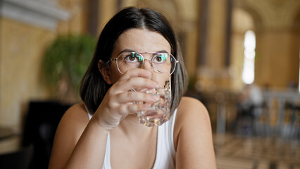 Young beautiful hispanic woman drinking a glass of water at cafeteria