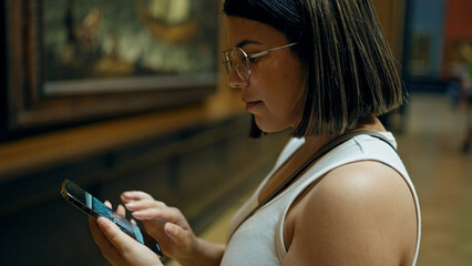 Young beautiful hispanic woman visiting art gallery using smartphone at Art Museum in Vienna
