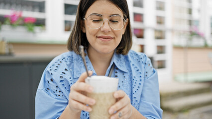 Young beautiful hispanic woman drinking coffee sitting on the table at outdoors cafeteria