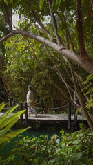 A woman strolls across a wooden bridge surrounded by lush greenery at a tropical balinese resort.
