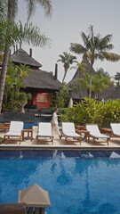 A woman strolls by the pool at a luxurious bali resort surrounded by palm trees and sun loungers.