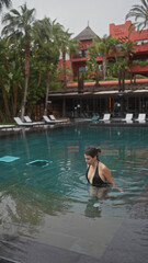 A young woman enjoys a serene moment in an infinity pool at a luxury resort in bali, surrounded by...