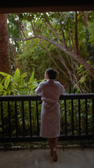 Rear view of a thoughtful woman in a bathrobe enjoying the serene bali resort terrace surrounded by...