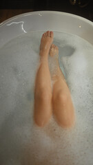 A woman relaxes in a bubble bath, legs visible, creating a serene indoor spa experience at home.