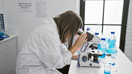 A focused hispanic woman scientist using a microscope in a modern laboratory setting.