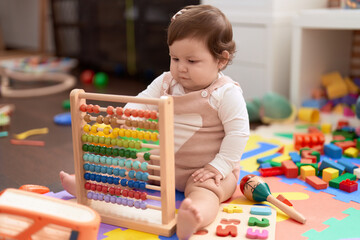 Adorable toddler playing with abacus sitting on floor at kindergarten