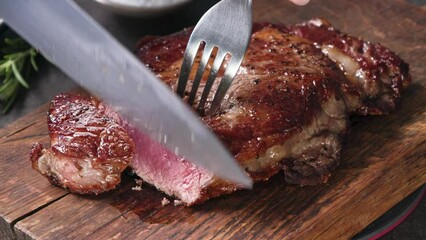 Chef slicing freshly grilled juicy beef steak meat with a knife on a wooden cutting board in the kitchen, food close-up zoom in