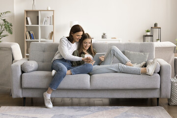 Cheerful mom teaching teen daughter child to use online app on tablet. Positive mother and...