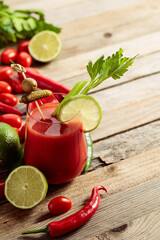 Bloody Mary cocktail garnished with gherkin, olive, lime, and celery on an old wooden table.