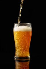 Pouring beer into a glass on a black reflective background.