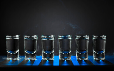 Alcoholic shots of vodka or strong drink in small glasses on a black background.