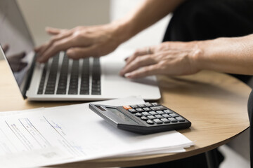 Cropped shot of senior woman doing accountant job, using financial application, online service laptop for payment on Internet, working with legal paper documents at home