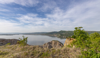 lakeside scene with a rocky cliff in the foreground. The cliff overlooks a calm lake with lush...