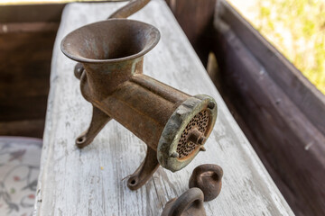 rusted cast iron manual meat grinder resting on a weathered wooden table with white paint.The metal...