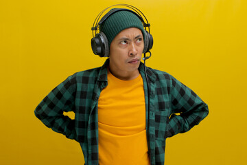 Asian man in a casual clothes, wearing headphones, looks up in deep thought, seemingly troubled by...