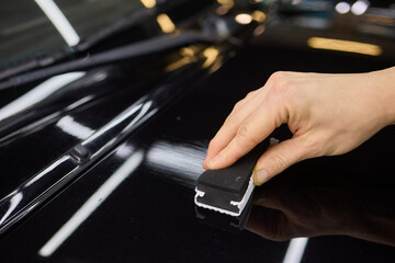Hand gestures polishing black car hood with sponge