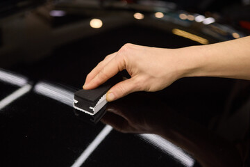 Hand gestures polishing black car hood with sponge