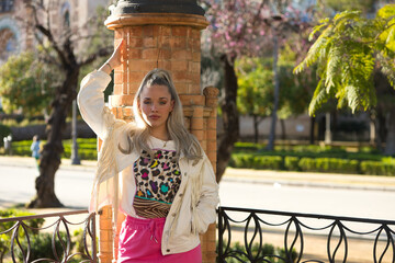Pretty young blonde woman with a ponytail in her hair leaning on a brick column seen in a Seville...