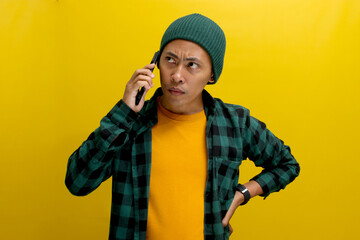 Serious young Asian man, dressed in beanie hat and casual shirt, listens intently to a serious...