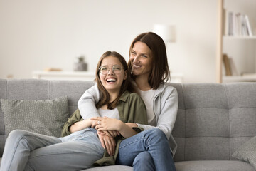 Happy mom and teenager daughter home casual portrait. Mother and teen girl resting on home sofa,...