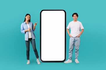 Korean young woman and man points at a massive, vertically oriented smartphone screen with a blank...