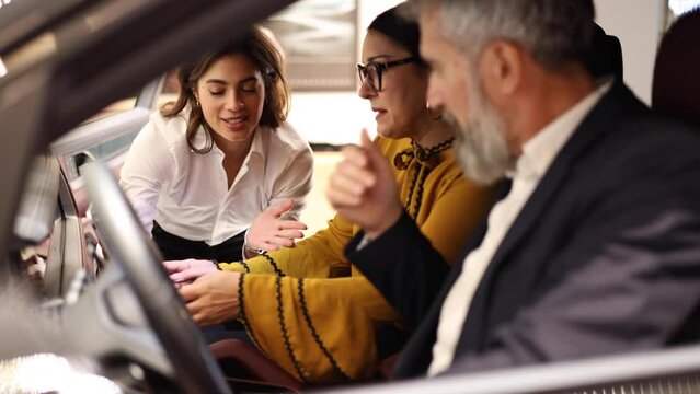 Female car seller showing the car interior to a mature couple