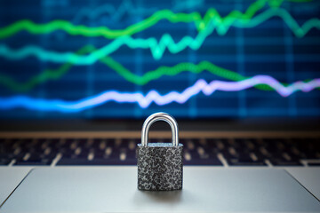 Close-up of a metal lock standing on a laptop against the background of a screen with a chart of stock quotes on the stock exchange.