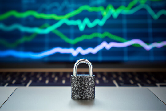 Close-up of a metal lock standing on a laptop against the background of a screen with a chart of stock quotes on the stock exchange.