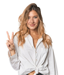 Caucasian blonde woman in studio showing victory sign and smiling broadly.