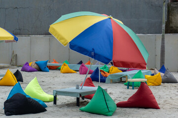 tent on the beach, Brightly colored beach umbrellas tilting in the wind, ottomans and tables at a...