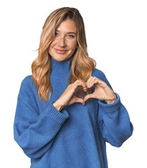 Caucasian blonde woman in studio smiling and showing a heart shape with hands.