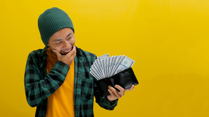 Thoughtful Asian man holds a wallet filled with cash contemplating how to spend it wisely, focusing...