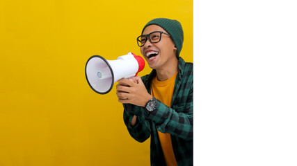 Excited Asian man in a beanie hat and casual shirt hides behind a white wall with blank space,...