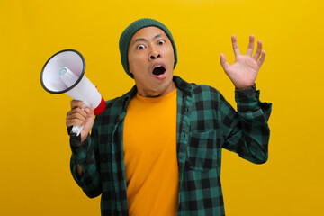 Excited Asian man in a beanie hat and casual shirt holding a megaphone announces a discount sale...