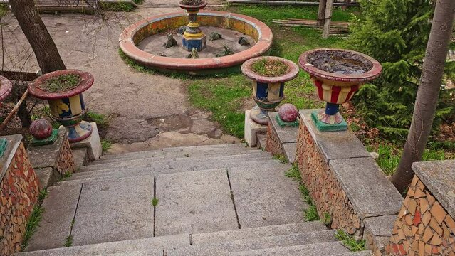 Descending old soviet public Issyk-Ata garden stairs with ornate vases and non-functional fountain at summer day in Kyrgyzstan.