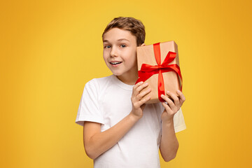 A boy, young in age, holding a wrapped present box in his hands, expressing excitement and...