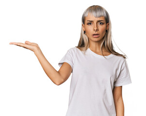 Young caucasian young woman in studio impressed holding copy space on palm.
