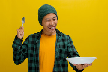 Excited young Asian man, sporting a beanie hat and casual shirt, holds a spoon while gazing at an...