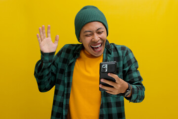 Happy Asian man wearing a beanie hat and casual shirt smiles broadly, displaying excitement and...