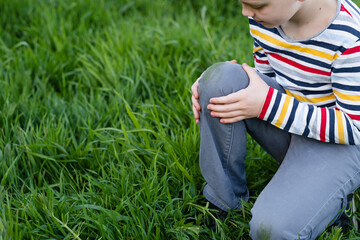 Dirty grass stains on clothes. The child at looking on knee sitting on one knee on a green...
