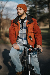 Stylish young man in casual attire enjoying his free time outdoors with his bike in a city park.