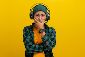 Asian man in a beanie and casual clothes, deep in thought with pensive expression while listening...