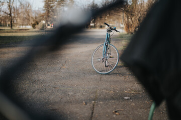 A single blue bicycle parked on an empty pathway, with autumn leaves scattered around and nature in the background.