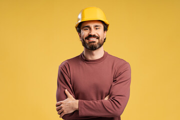 Portrait of handsome smiling architect with arms crossed wearing yellow hard hat, isolated