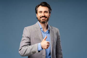 Smiling man in jacket showing thumbs up as symbol of like, looking at camera, isolated on blue