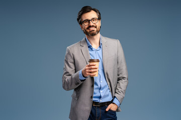 Happy businessman in glasses posing in studio, holding cup of coffee, looking at camera